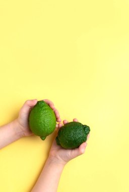 Two lemons lime in children's hands on a yellow background