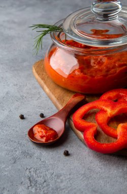 Gri arka planda cam bir kavanozda Ajvar
