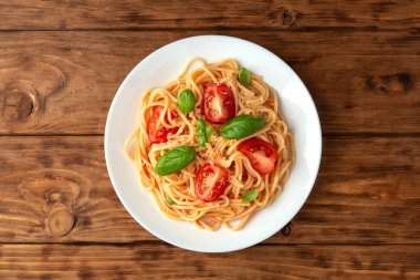 Tahta arka planda peynirli ve fesleğenli domates soslu makarna. Yukarıdan görüntüle