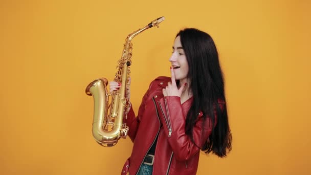 Schöne junge Frau schaut, zeigt Zeigefinger zur Seite und hält Saxophon — Stockvideo