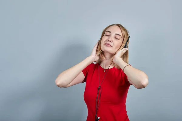 Mulher sorridente mantendo os olhos fechados, ouvir música, colocar as mãos em fones de ouvido — Fotografia de Stock