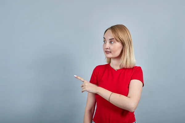Νεαρή γυναίκα με χειρονομίες, δείχνοντας τον δείκτη στην άκρη απομονωμένο στον γκρίζο τοίχο — Φωτογραφία Αρχείου