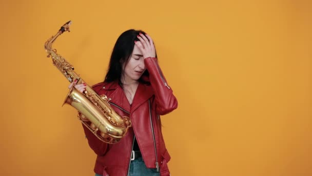 Attraktive junge Dame mit goldenem Saxophon posiert isoliert an gelber Wand — Stockvideo