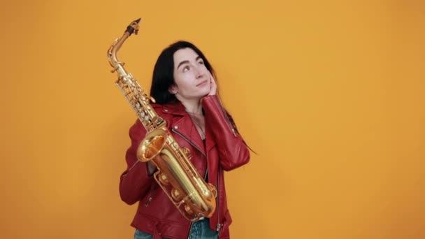 Mujer joven bonita mirando hacia arriba, poniendo la mano en la mejilla manteniendo saxofón — Vídeos de Stock