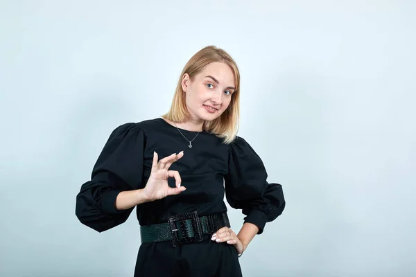 Blonde young woman wearing black dress looking camera showing OK gesture . — Stock Photo, Image