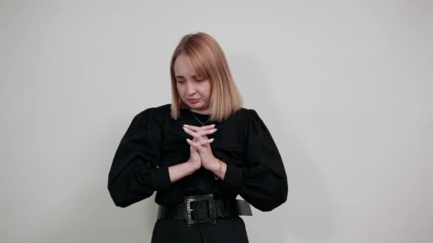 Νεαρή γυναίκα με έντονα καθημερινά ρούχα κοιτάζει κάτω, κρατώντας τα χέρια σταυρωμένα, προσεύχεται — Αρχείο Βίντεο