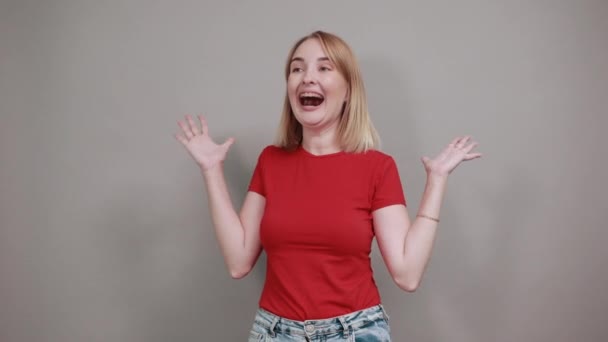 Aantrekkelijke jonge vrouw in rood shirt uitziende camera geïsoleerd op grijze muur — Stockvideo