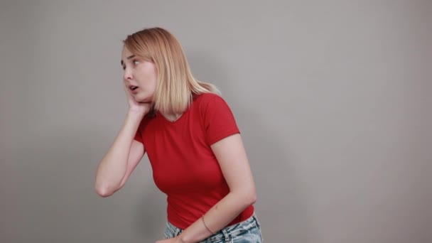 Portret jonge vrouw in rood shirt luistervink met gehoor gebaar, kijken opzij — Stockvideo