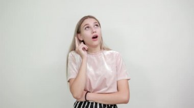 İzole edilmiş beyaz duvarın üzerindeki genç kadın parmağını uzatıyor, yukarı bakıyor.