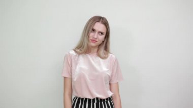 Pastel gömlekli, kameraya bakan, ellerini açan neşeli genç bir kadın.