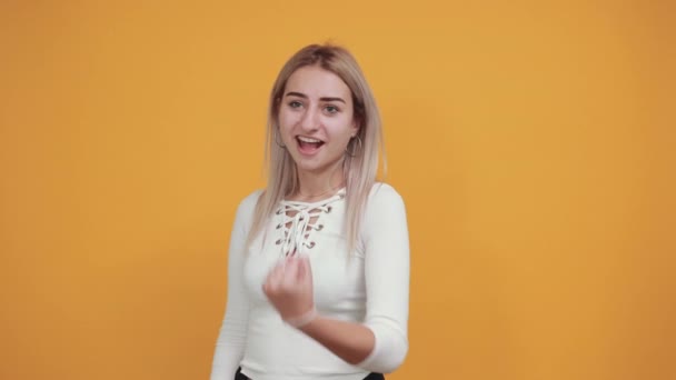 Junge Frau sieht so lustig aus, über orangefarbene Wand glücklich und zeigt zur Seite — Stockvideo