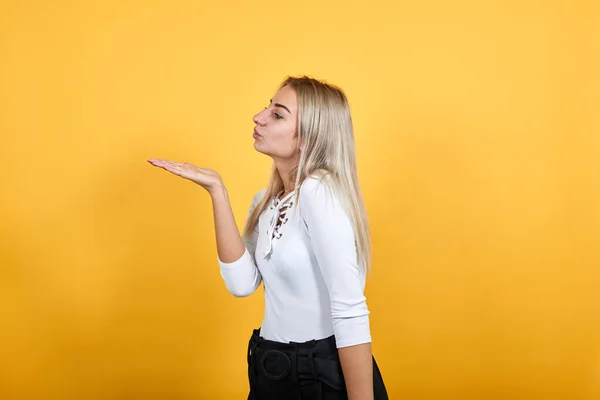 Söt ung kvinna i vit skjorta skicka luft kyss åt sidan isolerad på orange vägg — Stockfoto