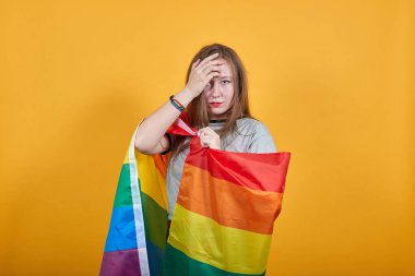 Rahat kadın gözlerini açık tutuyor, elleri başının arkasında, Lbgt bayrağını kapatıyor.