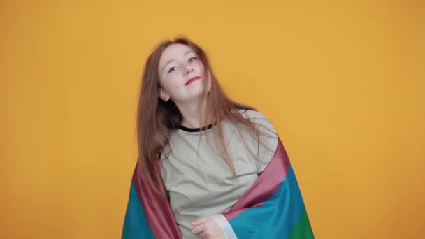 Красивая молодая девушка над изолированной оранжевой стеной держит кулак вверх, прикрывая флаг ЛГБТ — стоковое видео