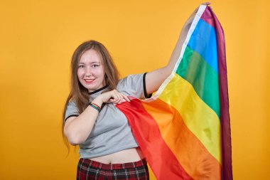 Çekici bir genç kadının portresi kameraya bakıyor, Lgbt bayrağı sallıyor.