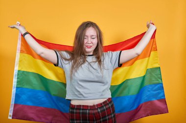 Pastel tişörtlü gülümseyen genç kadın, ellerini kaldırıyor, Lgbt bayrağını örtüyor.