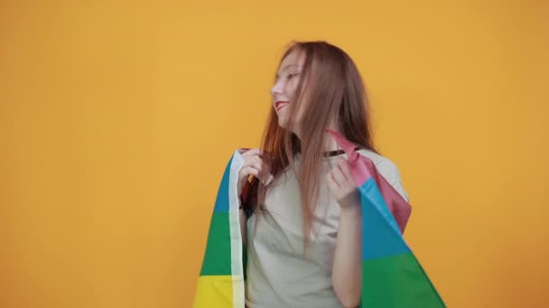 Mujer caucásica joven que sufre dolor en las manos, con aspecto de miedo, cubierta bandera LGBT — Vídeo de stock