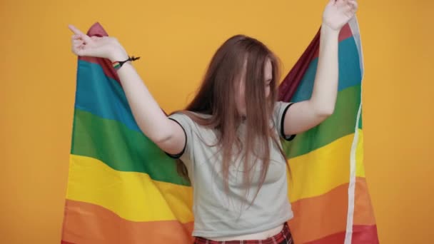 Усміхнена молода жінка в пастельній сорочці тримає руки вгору, прикриває прапор ЛГБТ — стокове відео