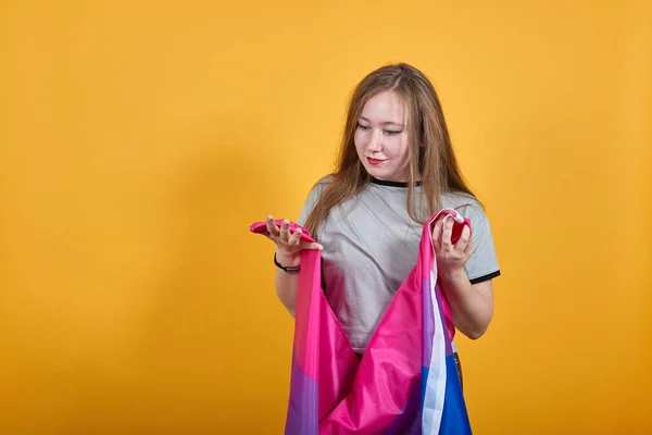 Mladá žena shlíží dolů, roztahuje ruce zakryté bisexuální vlajkou — Stock fotografie