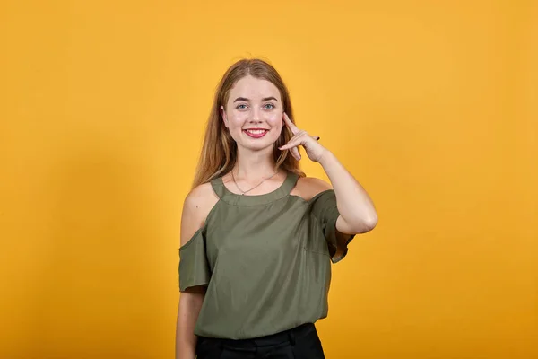 Portret van een jonge vrouw in een haki oranje shirt met een vinger op de wang, glimlachend — Stockfoto