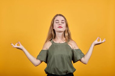 Günlük kıyafetli genç bir kadın yoga jestinde el ele tutuşur, meditasyon yaparken rahatlar..