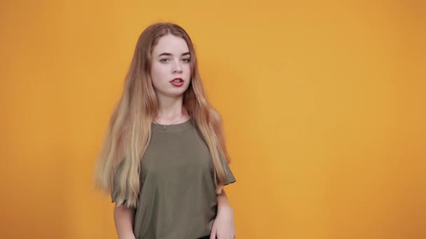 Chica sobre la pared naranja haciendo un gesto sin importancia parada, mirando directamente — Vídeo de stock