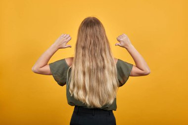 Esmer, genç bir kadının arkası. Başparmaklarıyla kendini işaret ediyor.