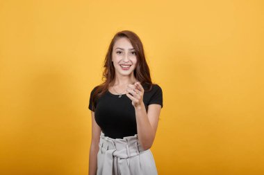 Genç ve güzel bir kadın işaret parmağını kameraya doğrultup gülüyor.