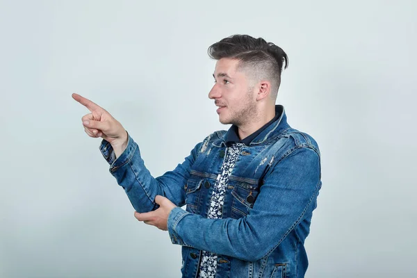 Hombre guapo en chaqueta de mezclilla de moda apuntando hacia un lado, espacio para la publicidad — Foto de Stock