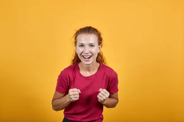 Όμορφη νεαρή κοπέλα με κόκκινο πουκάμισο κάνει χειρονομία νικητή, χαμογελώντας, κρατώντας γροθιές επάνω — Φωτογραφία Αρχείου