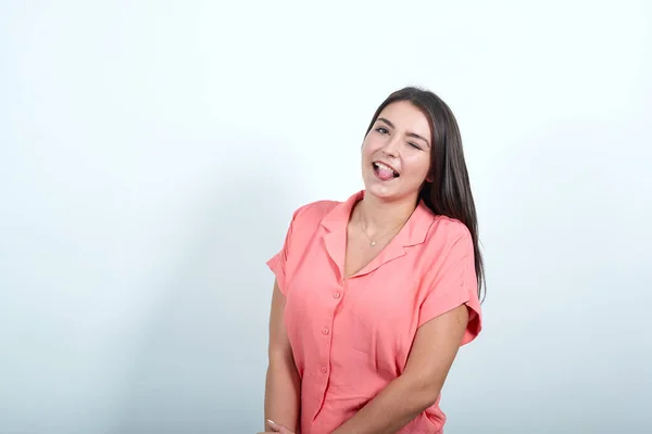 Giovane donna sul muro bianco mostrando la lingua alla fotocamera con sguardo divertente — Foto Stock