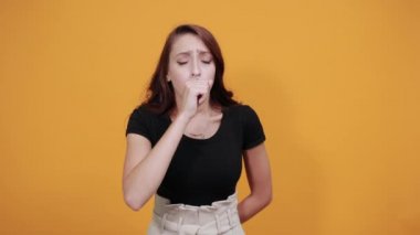 Siyah gömlekli çekici genç bir kadın, hasta görünüyor, öksürüyor, elleri ağızda.