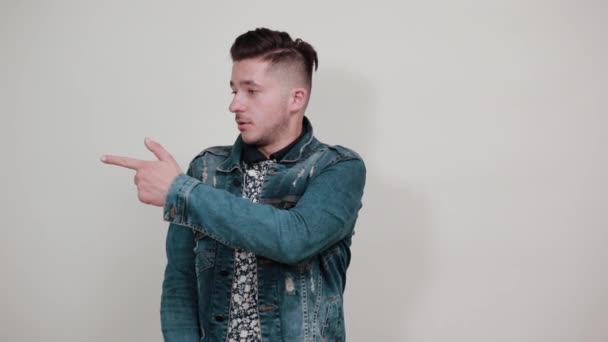 Mladý pohledný muž v módní bundě ukazuje stranou na prostor pro reklamu — Stock video
