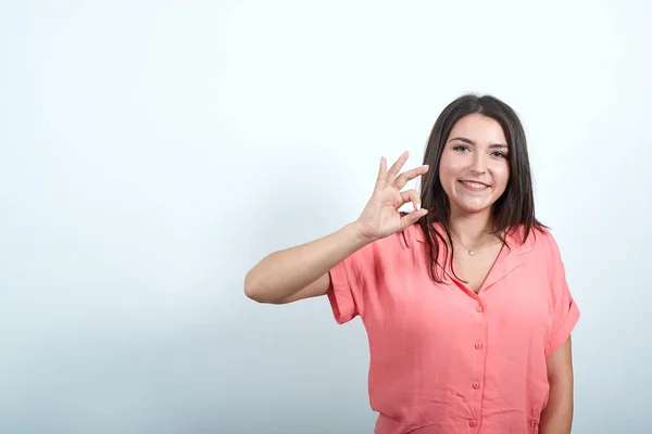 Fröhliche kaukasische junge Frau im rosafarbenen Hemd zeigt okay Geste, lächelt — Stockfoto