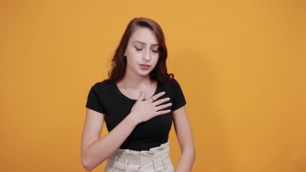 Привлекательная серьезная молодая женщина в черной рубашке держит руки на груди, сердце — стоковое видео