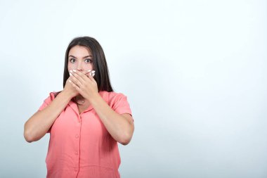 Şok olmuş pembe gömlekli kadın elleri ağızda, korkmuş görünüyor.