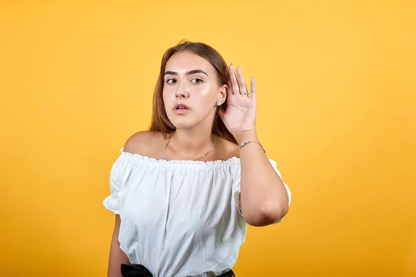 Attraktive junge Frau hält Hand an Ohren, Klatschkonzept an orangefarbener Wand — Stockfoto