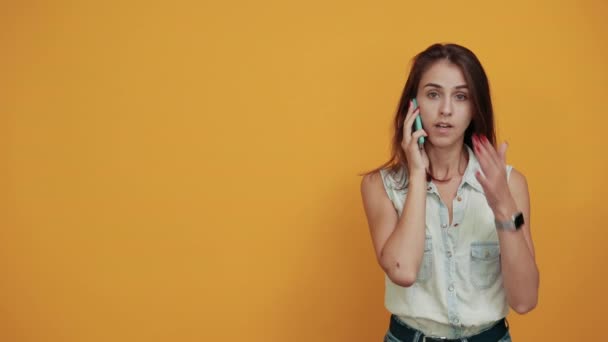 Woman keeping hand on mouth, holding telephone, speaking about something — Stock Video