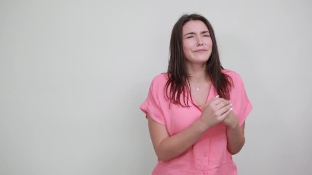 Vonzó fiatal nő rózsaszín ingben, csukott szemmel. Ökölbe szorítva — Stock videók