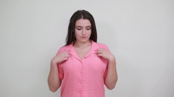 Весела біла жінка в рожевій сорочці спрямовує пальці на себе, посміхаючись — стокове відео