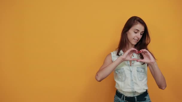 Attractive young woman in blue denim shirt showing shape of heart gesture — 图库视频影像