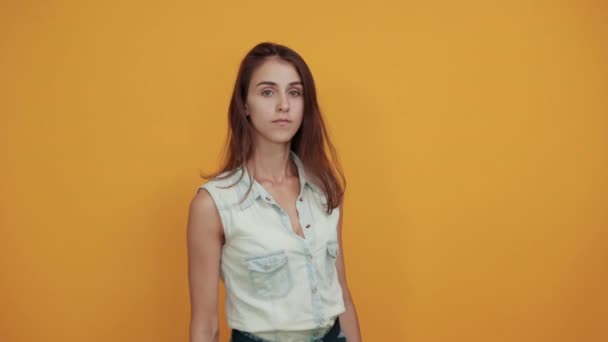 Mujer joven caucásica estricta en camisa de mezclilla azul permaneciendo a un lado en la pared naranja — Vídeo de stock