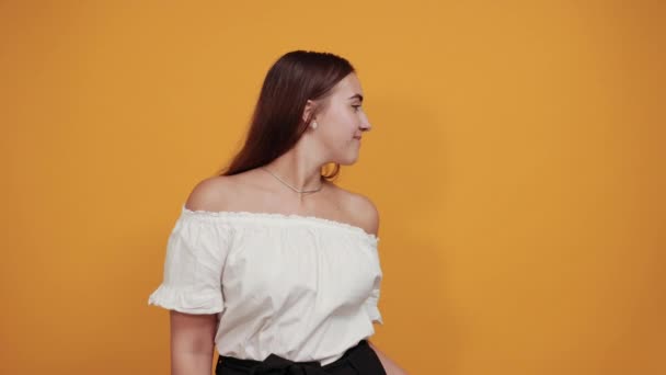 Glada kaukasisk ung kvinna ler, pekar på kameran orange vägg. — Stockvideo