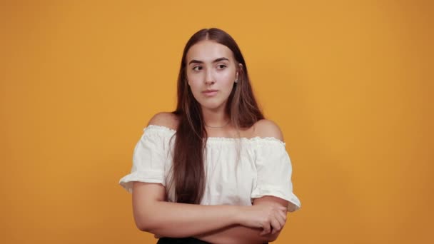 Ung munter kvinde peger til side, smilende isoleret på orange væg – Stock-video