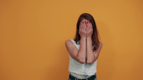 Chockad kvinna i denim skjorta täcker ögon med händer, tittar genom fingrar — Stockvideo
