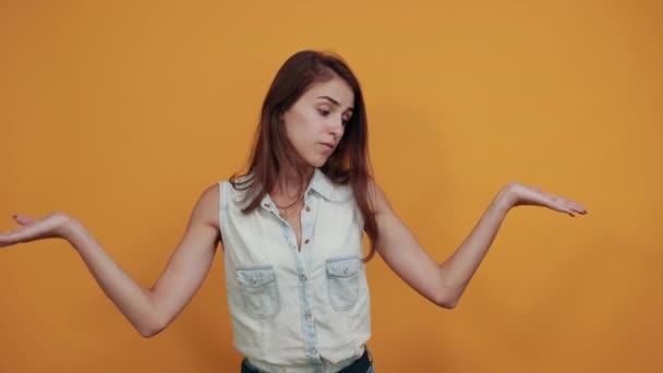 Μπερδεμένη λευκή νεαρή γυναίκα απλώνει τα χέρια της απομονωμένα στον πορτοκαλί τοίχο. — Αρχείο Βίντεο