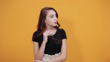 Siyah tişörtlü, elinde güneş gözlüğü olan heyecanlı genç kız yan bakıyor.