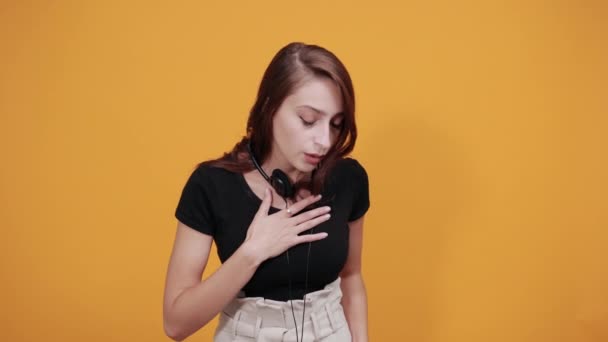 Trött dam med hörlurar på halsen, ser sjuk ut, håller hand på bröstet — Stockvideo