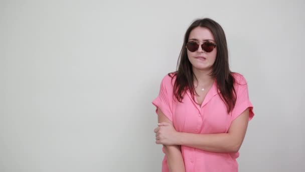 Модна жінка в рожевій сорочці тримає руку на підборідді, посміхається, має сонцезахисні окуляри — стокове відео