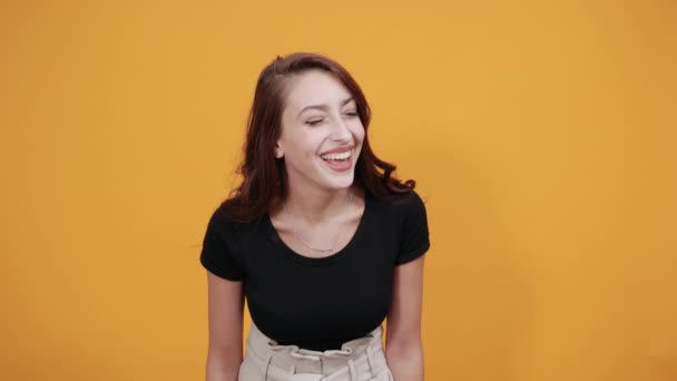 Приваблива молода жінка в чорній сорочці, посміхаючись, тримає руку на грудях — стокове відео